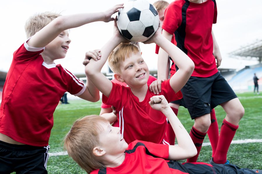 Junge Kinden in Fußballtrikots auf einem Platz halten gemeinsam einen Ball hoch